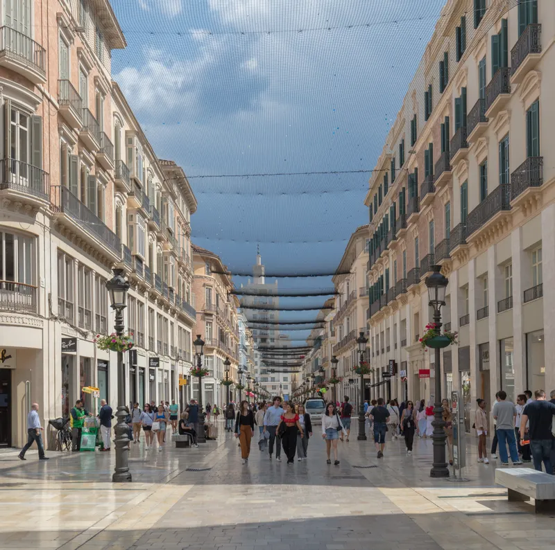 Pedestrian Calle Larios with its 19th-century buildings, canvas awnings between the façades and people strolling.